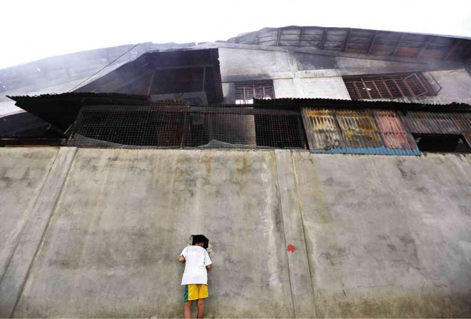 A boy peers through a hole in a wall that was made by firefighters for their hoses to reach further into the Kentex footwear factory in Valenzuela when it burned down on May 13. PHOTO BY RAFFY LERMA 
