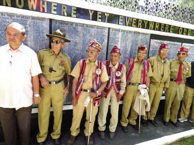Veterans, with Jose, stand in front of a wall listing the names of Baguio and Cordillera WWII fighters.
