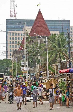 DISPLACED residents spill into the streets as police-backed demolition workers begin tearing down an informal settler colony within a prime commercial area in Quezon City, which includes the ABS-CBN building and the castle-like Camelot Hotel (background).