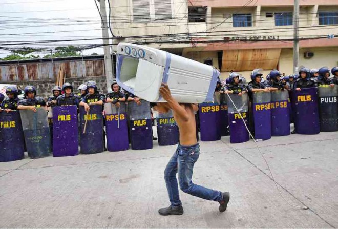 NO CLEAN EXIT Saving his washing machine, an evicted resident walks past a line of antiriot policemen sent to secure a squatter colony up for demolition on Tuesday in Barangay South Triangle, Quezon City.  PHOTOS BY LYN RILLON 