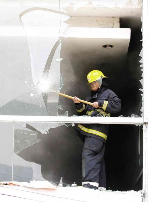 A FIREMAN shatters glass windows to let out the smoke inside the Victory Mall in Caloocan City which caught fire  Monday. LYN RILLON