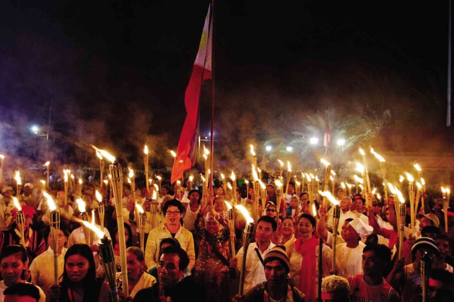 APO Reyna Yolanda Liban Manalo, founder of Celyo Rizal, raises the Philippine flag amid torches held by leaders and members of various groups of Rizalistas, together with local government officials, during a ceremony held at the foot of the 7-meter-tall Rizal statue in Calamba City, Laguna, hours before midnight on June 18. The province celebrated the national hero’s 154th birth anniversary. CHRIS QUINTANA/CONTRIBUTOR 