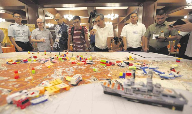 RESPONSE PLAN FOR EARTHQUAKE AND TSUNAMI  National Disaster and Risk Reduction Council Executive Director Alexander Pama (5th from left) discusses contingency plans for a massive earthquake and a resulting tsunami that could hit Metro Manila. Key supports groups, marked by miniature toys, are placed on an enlarged map of the metropolis during the Table-Top Exercise National Disaster Response Plan Earthquake and Tsunami meeting in Camp Aguinaldo, Quezon City. LYN RILLON