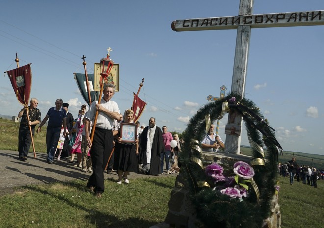 A religious procession passes an Orthodox cross with a sign reading Save and Guard at the crash site of the Malaysia Airlines Flight 17, near the village of Hrabove, eastern Ukraine, Friday, July 17, 2015. Residents of the Ukrainian village where the Malaysian airliner was shot down with 298 people aboard a year ago began a procession to the crash site on Friday, while the Australian prime minister remembered the savagery of the disaster by unveiling a plaque in Canberra thats set in soil from the place where the plane went down. (AP Photo/Mstyslav Chernov)