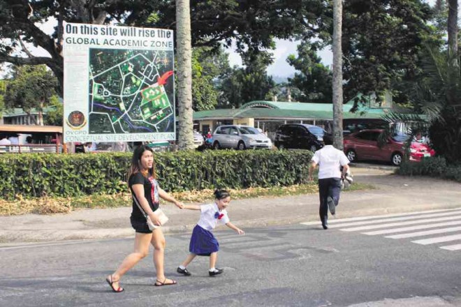 A PUPIL of Maquiling School Inc. (MSI) pulls her mother as they cross the street. Behind them is the signage announcing that the University of the Philippines Los Baños, to which MSI is leasing the property, is putting up a “global academic zone” on the site. CLIFFORD NUÑEZ/CONTRIBUTOR 