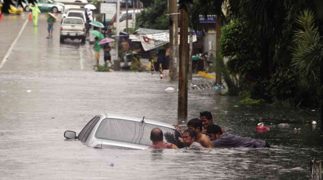 TOO LATE  Residents try to move a car submerged on Mother Ignacia Avenue, Quezon City, as the road goes underwater within minutes during a downpour on Wednesday. EDWIN BACASMAS