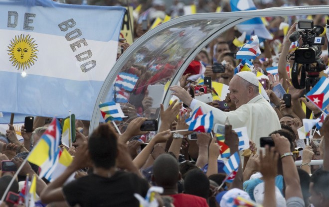 Pope Francis arrives for Mass at Revolution Plaza in Havana, Cuba, Sunday, Sept. 20, 2015, where people wave Cuban, Vatican and Argentine flags. Pope Francis opens his first full day in Cuba on Sunday with what normally would be the culminating highlight of a papal visit: Mass before hundreds of thousands of people in Havana's Revolution Plaza. (AP Photo/Ramon Espinosa)