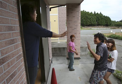 In this Friday, Sept. 4, 2015 photo, Naoko Kanai, left, waves to her neighbor Koji Matsuimoto, second from right, from her house after they returned home for the first time in about two months, in Naraha town, Fukushima prefecture, northeastern Japan. This past weekend, Naraha became the first of seven towns that had been entirely evacuated to reopen since the March 11, 2011, disaster, when a tsunami slammed into the Fukushima Dai-ichi nuclear power plant, causing meltdowns and a massive radiation leak. Kanai, a 50-year-old homemaker, is among those having trouble deciding whether to return to Naraha permanently. (AP Photo/Koji Sasahara)