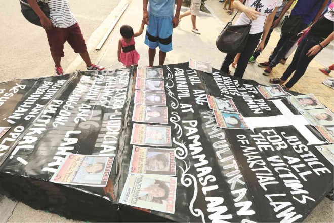 VICTIMS OF MARTIAL LAW A child looks at a big mock coffin painted with slogans and bearing pictures of people who disappeared during the military rule of President Ferdinand Marcos. The human rights group Karapatan and Bagong Alyansang Makabayan in Southern Tagalog displayed the coffin on the grounds of Baclaran Church in Parañaque City on Sunday, the eve of the 43rd anniversary of the declaration of martial law. JILSON SECKLER TIU