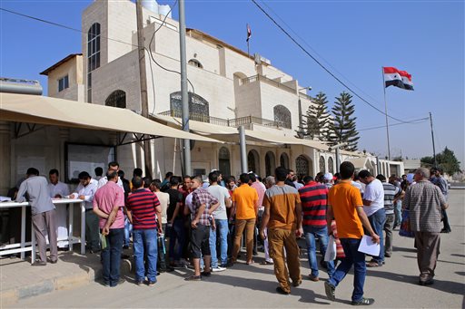 In this Tuesday, Sept. 15, 2015 photo, Syrian refugees gather outside their embassy waiting to apply for passports or to renew their old ones, in Amman, Jordan. Hundreds of Syrian refugees line up at their country's embassy every day for a long shot at a better future in Europe: They apply for Syrian passports that can get them into Turkey without visas, and from there plan to start dangerous journeys by sea and land to the continent. (AP Photo/Raad Adayleh)