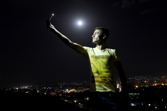 In this picture taken on September 27, 2015, an Afghan man is illuminated by the light from his phone while taking a selfie on the top of the Wazir Akbar Khan hill in Kabul, as a view of the "supermoon" is seen in the background. For the first time in decades, skygazers are in for the double spectacle on September 28 of a swollen "supermoon" bathed in the blood-red light of a total eclipse. The celestial show, visible from the Americas, Europe, Africa, west Asia and the east Pacific, will be the result of the Sun, Earth and a larger-than-life, extra-bright Moon lining up for just over an hour from 0211 GMT.    AFP PHOTO / Wakil Kohsar