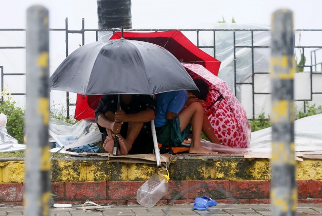 Residents huddle together under their umbrellas as strong winds and slight rain are brought by Typhoon Koppu Sunday, Oct. 18, 2015 in Manila, Philippines. The slow-moving typhoon blew ashore with fierce wind in the northeastern Philippines early Sunday, toppling trees and knocking out power and communications. Officials said there were no immediate reports of casualties. (AP Photo/Bullit Marquez)