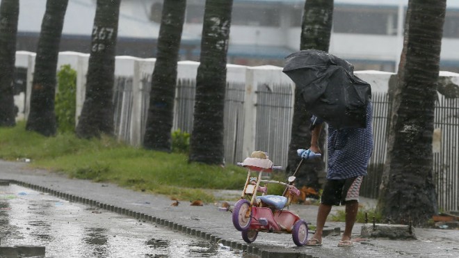 A man retrieves a baby tricycle under strong winds and slight rain brought by Typhoon Koppu Sunday, Oct. 18, 2015 in Manila, Philippines. The slow-moving typhoon blew ashore with fierce wind in the northeastern Philippines early Sunday, toppling trees and knocking out power and communications. Officials said there were no immediate reports of casualties. (AP Photo/Bullit Marquez)