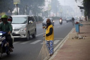 A woman wears a mask due to the haze as she sweeps the street in Palembang, South Sumatra, Indonesia, Friday, Sept. 18, 2015. Indonesian police said Thursday they have identified seven companies and 133 individuals suspected of causing forest fires that are spreading choking smoke and polluted air across parts of western Indonesia and neighboring Malaysia and Singapore. (AP Photo/Tatan Syuflana)