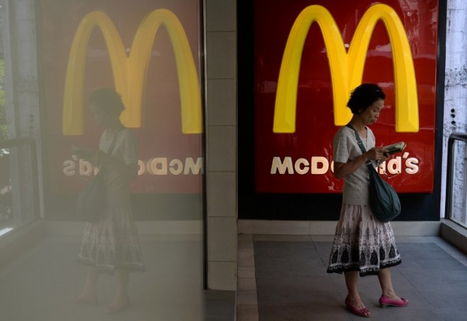 A woman reads outside a McDonald's fastfood restaurant in Hong Kong on July 28, 2014.  McDonald's in Hong Kong on July 24 suspended sales of chicken nuggets and several other items including chicken burgers, salads and lemon tea after admitting it imported food from a US-owned firm in China at the centre of an expired meat scandal.  McDonald's outlets in Beijing and Shanghai, it was reported on July 28, have yanked their flagship burgers off the menu after a key US supplier recalled products made by its Shanghai factory, which is alleged to have used expired meat.       AFP PHOTO / DALE DE LA REY