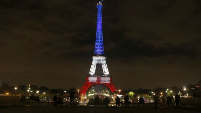 People look at the Eiffel Tower illuminated in the French colors in honor of the victims of the attacks on Friday in Paris, Monday, Nov. 16, 2015. France is urging its European partners to move swiftly to boost intelligence sharing, fight arms trafficking and terror financing, and strengthen border security in the wake of the Paris attacks. (AP Photo/Frank Augstein)