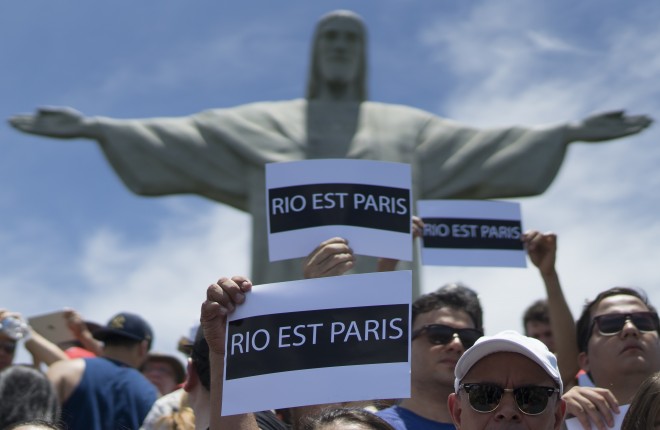 People hold up signs that read in French: "Rio is Paris" during a demonstration promoted by the NGO Rio de Paz, in solidarity with the victims of the attacks in Paris in front of Christ the Redeemer statue, in Rio de Janeiro, Brazil, Saturday, Nov. 14, 2015. French officials say several dozen people died Friday night when attackers launched gun attacks at Paris cafes, detonated suicide bombs near France's national stadium and killed hostages inside a concert hall during a rock show. More than 200 people were injured, dozens critically. (AP Photo/Leo Correa)