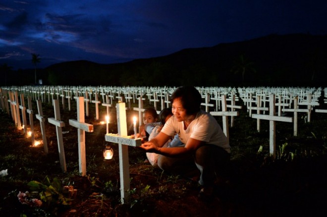A woman, accompanied by her young family members, writes the name of a loved one on a cross at a mass graveyard for victims of typhoon Haiyan during All-Saints' Day in Tacloban City, Leyte province, central Philippines on November 1, 2015. Millions of people in the Philippines made their annual pilgrimages to family gravesites on November 1 in a tradition that combines fervent Catholic faith with the country's penchant for festivity, but in the central city of Tacloban, which is still suffering the devastation of Super Typhoon Haiyan, the mood was mournful and sombre. Many of the mourners had to visit a mass grave where more than 2,400 bodies were interred after Haiyan, the strongest typhoon ever recorded to hit land, ravaged the city in November 2013.  AFP PHOTO / TED ALJIBE