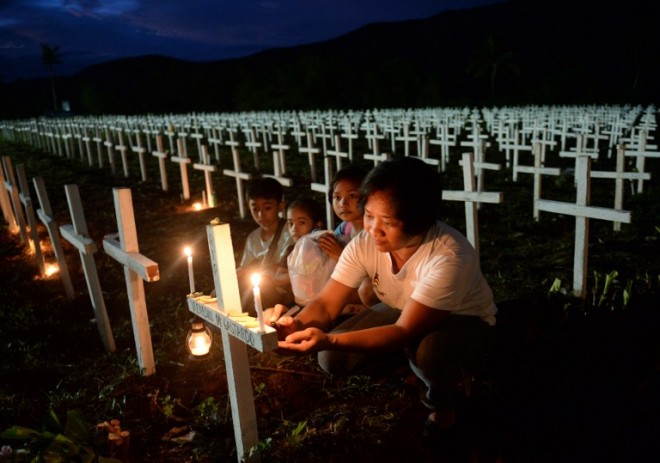 A woman, accompanied by her young family members, writes the name of a loved one on a cross at a mass graveyard for victims of typhoon Haiyan during All-Saints' Day in Tacloban City, Leyte province, central Philippines on November 1, 2015. Millions of people in the Philippines made their annual pilgrimages to family gravesites on November 1 in a tradition that combines fervent Catholic faith with the country's penchant for festivity, but in the central city of Tacloban, which is still suffering the devastation of Super Typhoon Haiyan, the mood was mournful and sombre. Many of the mourners had to visit a mass grave where more than 2,400 bodies were interred after Haiyan, the strongest typhoon ever recorded to hit land, ravaged the city in November 2013.  AFP PHOTO