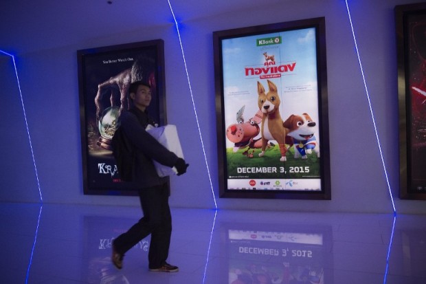 This photo taken on December 9, 2015 shows a man walking next to a poster (R) for the film "Khun Tongdaeng: The Inspiration" at a cinema in Bangkok. The animated film based on the Thai King's favourite dog, a potent symbol used by the monarch through stories to dispense advice to the nation, has this week shot to number two at the box office.      AFP PHOTO / Nicolas ASFOURI / AFP / NICOLAS ASFOURI
