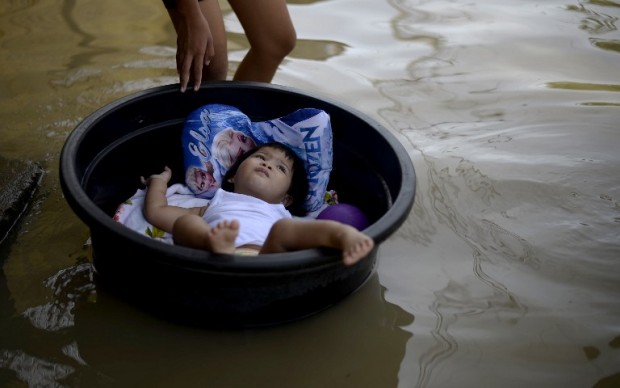 In this photo taken on December 24, 2015, a child lies in a plastic wash basin along a flooded street in Calumpit Bulacan, north of Manila. Residents in typhoon-hit Philippine villages have little to celebrate this Christmas as towns in the vast, rice-growing central Luzon plains near Manila remain submerged with the government saying some 206,000 people are still either stuck in floods or dependent on government food rations, or both.  AFP PHOTO 