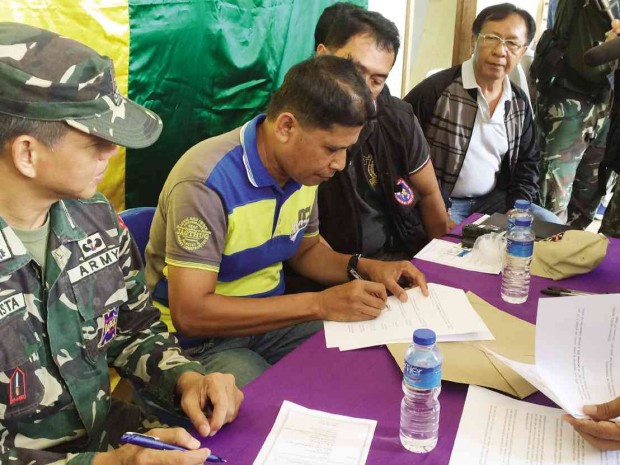 IN A SHOW of cooperation, Moro Islamic Liberation Front ’s 114th Base Command chief Dan Asnawi (in yellow and blue striped shirt) signs a document committing to work with the military, local government and International Monitoring Committee to secure communities liberated from the Abu Sayyaf Group. JULIE ALIPALA/INQUIRER MINDANAO