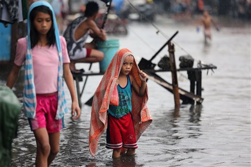 A Filipino boy uses a towel to cover himself from rain caused by Typhoon Melor as he crosses a flooded street outside their homes in suburban Navotas, north of Manila, Philippines on Wednesday, Dec. 16, 2015. AP PHOTO