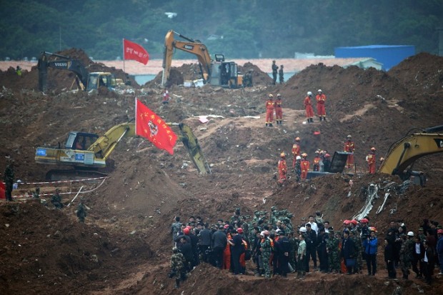 In this Dec. 22, 2015 photo, government officials led by head of the rescue units look at the rescuers conducting search and rescue operation following a landslide at an industrial park in Shenzhen, in south China's Guangdong province. Police in southern China say a local government official has killed himself, a week after a landslide from a pileup of construction waste in his city left scores missing and presumed dead. A statement from the Shenzhen police said the head of the Urban Management Bureau in the city's Guangming New District jumped to his death from a building Sunday, Dec. 27, 2015. (AP Photo/Andy Wong)