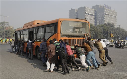 Passengers and traffic policemen push a bus after it broke down at a traffic intersection on the first day of a two-week experiment to reduce the number of cars to fight pollution in New Delhi, India, Friday, Jan. 1, 2016. (AP Photo/Altaf Qadri)