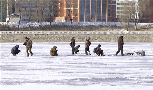 In this Monday, Jan. 18, 2016, image made from Associated Press Television News video, North Koreans stand on the frozen Taedong River as a man, right, ice fishes in Pyongyang, North Korea. The depths of winter have hit North Korea, with temperatures dropping lower than last year. (Associated Press Television News via AP)