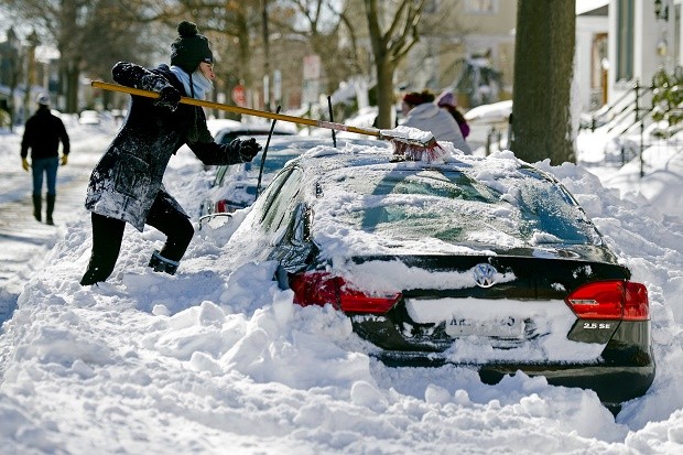 Rhianna McCarte, 30, clears snow from her car, before digging it out, in Alexandria, Va., Sunday, Jan. 24, 2016. Millions of Americans were preparing to dig themselves out Sunday after a mammoth blizzard with hurricane-force winds and record-setting snowfall brought much of the East Coast to an icy standstill. (AP Photo/Cliff Owen)