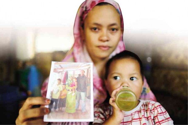 FATIMA Sandigan, 39, widow of a Moro Islamic Liberation Front fighter, shows a family picture as she holds her daughter inside their house in Tukanalipao, Mamasapano, Maguindanao province. JEOFFREY MAITEM