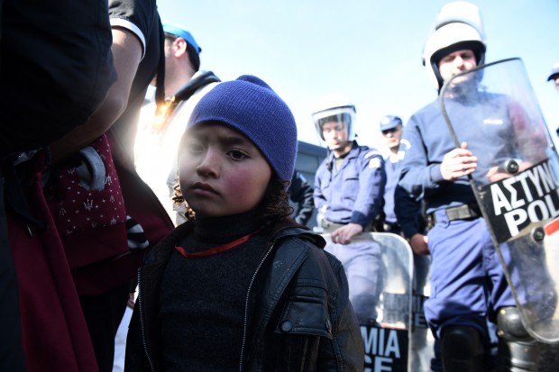 A girl stands in front of Greek policemen as they block the Greek-Macedonian borderline near the northern Greek village of Idomeni, Monday, Feb. 22, 2016. Greece's government warned Monday it expected a growing number of stranded migrants and asylum seekers after neighbor Macedonia further restricted border access at the weekend. (AP Photo/Giannis Papanikos)