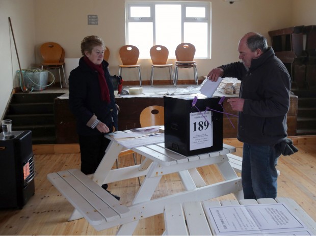 Presiding Officer Carmel McBride looks on as a resident casts his ballot as voting gets underway on the island of Inishbofin Ireland. People living on the remote isle  of Inishbofin off the coast of Donegal are among the first to cast their ballots in Ireland's General Election, a day ahead of the rest of the country.  (Niall Carson/PA Via AP)  UNITED KINGDOM OUT  NO SALES NO ARCHIVE