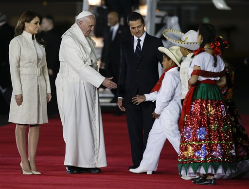 Pope Francis reaches out to greet youth dressed in traditional Mexican outfits as he's escorted by Mexico's President Enrique Pena Nieto, behind, and first lady Angelica Rivera, upon arrival to Benito Juarez International Airport in Mexico City, Friday, Feb. 12, 2016. The pontiff is in Mexico for a week-long visit. (AP Photo/Gregorio Borgia)