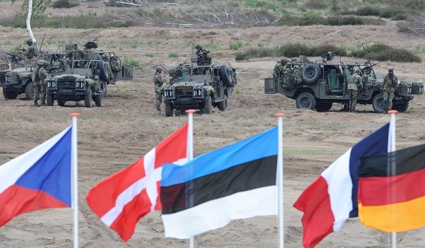 FILE - In this June 18, 2015,file photo flags wave in front of soldiers who take positions with their army vehicles during the NATO Noble Jump exercise on a training range near Swietoszow Zagan, Poland.  Poland said Wednesday Feb. 3, 2016 it welcomes  a U.S. plan to quadruple military spending in Europe in reaction to Russias military resurgence, yet the tone from several governments appears guarded as it remains unclear how much of the spending will translate into a real and lasting presence of troops and weapons on NATOs nervous eastern flank. (AP Photo/Alik Keplicz)