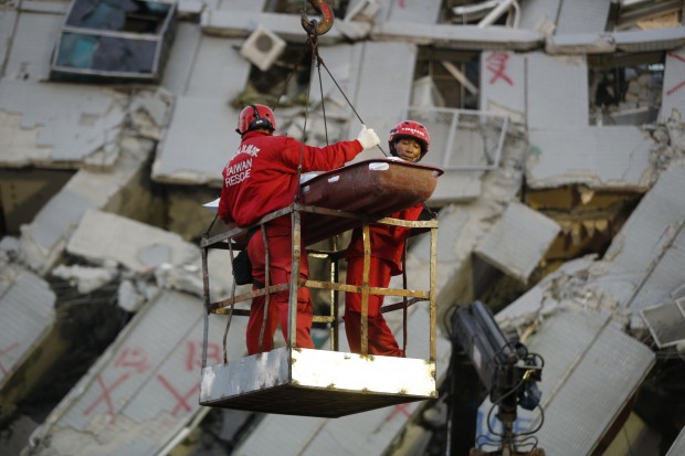 Two emergency workers carry a victim recovered from a collapsed building in Tainan, Taiwan, Sunday, Feb. 7, 2016. Rescuers on Sunday found signs of live within the remains of a high-rise residential building that collapsed in a powerful, shallow earthquake in southern Taiwan that killed over a dozen people and injured hundreds. (AP Photo/Wally Santana)