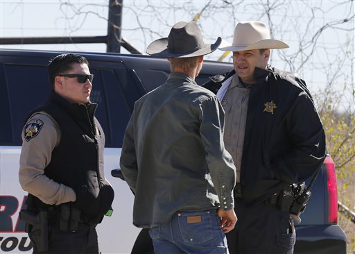 In this Saturday, Feb. 6, 2016 photo, Uvalde County Sheriffs Deputies talk with an individual while guarding the intersection to a neighborhood several miles outside of Uvalde after a standoff resulted in multiple deaths. The incident started on Friday.  (Kin Man Hui, San Antonio Express-News via AP) RUMBO DE SAN ANTONIO OUT; NO SALES; MANDATORY CREDIT