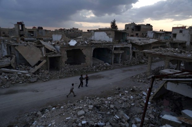 Syrian children walk past heavily damaged buildings in the rebel-held town of Douma, on the eastern edges of the capital Damascus on February 27, 2016, on the first day of the landmark ceasefire agreement.  Less than a day into a landmark ceasefire deal in parts of the country, residents say their usual routine has been thrown off without the usual sounds of artillery, rocket attacks, or helicopter-borne barrel bombs.  / AFP / Sameer Al-Doumy