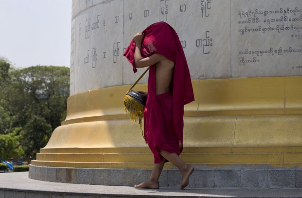 A novice Buddhist monk covers his head with his robe as he prepares to walk into the sun's rays in a hot humid day at a public park in Yangon, Myanmar, Thursday, March 17, 2016. In Yangon during the month of March, temperature rises up to 37 degrees Celsius (98 degrees Fahrenheit) with up to 94 percent humidity before the tropical rainy season starts in May. (AP Photo/Gemunu Amarasinghe)