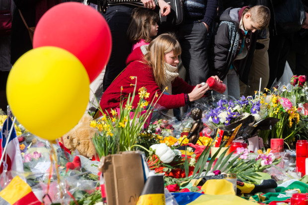 A woman lights a candle at floral tributes at a memorial site at the Place de la Bourse in Brussels, Saturday, March 26, 2016. Brussels airport officials say flights won't resume before Tuesday as they assess the damage caused by twin explosions in the terminal earlier this week. (AP Photo/Geert Vanden Wijngaert)
