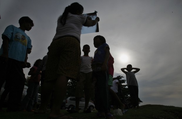 FILE  - In this Jan. 26, 2009 file photo, an Indonesian girl look up through an x-ray film sheet to watch an annular solar eclipse in the sky as people gather in Anyer Beach, Banten province, Indonesia. The rare and awe-inspiring spectacle of a total solar eclipse will unfold over parts of Indonesia and the Indian and Pacific Oceans on Wednesday, March 9, 2016, weather permitting. The full eclipse may be visible to several million people within its narrow path including eclipse chasers who have traveled from around the world for a chance to witness it. (AP Photo/Achmad Ibrahim, File)
