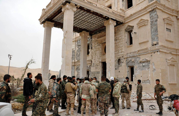 In this photo released on March 24, 2016, by the Syrian official news agency SANA, Syrian government soldiers gather outside a damaged palace, in Palmyra, central Syria. Syrian government forces recaptured a Mamluk-era citadel in Palmyra from the extremist Islamic State group on Friday, Syrian state media and monitoring groups said, as the fierce battle for control of the historic town entered its third day. (SANA via AP)