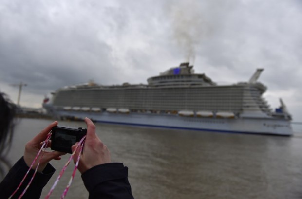 A woman takes a picture of the Harmony of the Seas cruise ship as it leaves the STX shipyard of Saint-Nazaire, western France, for a three-day offshore test, on March 10, 2016.  / AFP / LOIC VENANCE