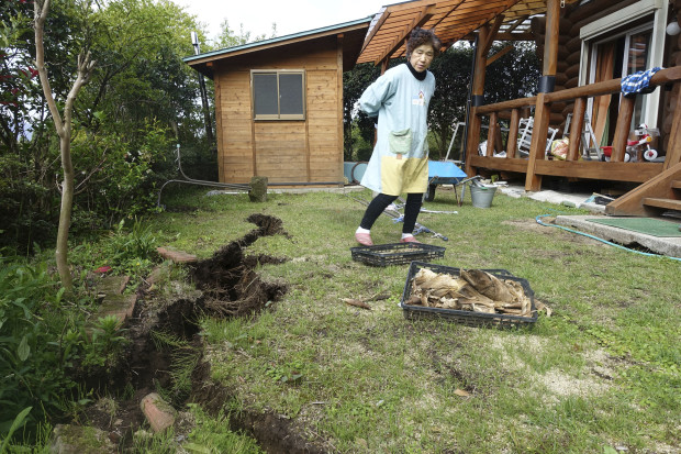 In this April 19, 2016 photo, Yachiyo Fuchigami, 64, wife of Koji Fuchigami, looks at the deep crack in the garden as the couple briefly returns home to check the extent of damage to their houses in Minamiaso, Kumamoto prefecture, Japan. A mountain village that attracted retirees, tourists and agriculture students to a college campus faces a grim future after last week's devastating earthquake. (AP Photo/Mari Yamaguchi)
