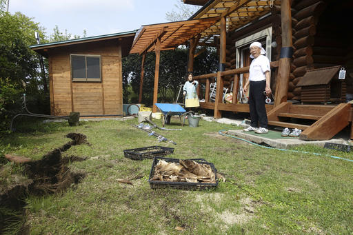 In this April 19, 2016 photo, Koji Fuchigami and his wife Yachiyo look at the damage on the ground as they briefly return home to pick up valuables and fresh clothes to take to their shelter in Minamiaso, Kumamoto prefecture, Japan. A mountain village that attracted retirees, tourists and agriculture students to a college campus faces a grim future after last week's devastating earthquake. (AP Photo/Mari Yamaguchi)