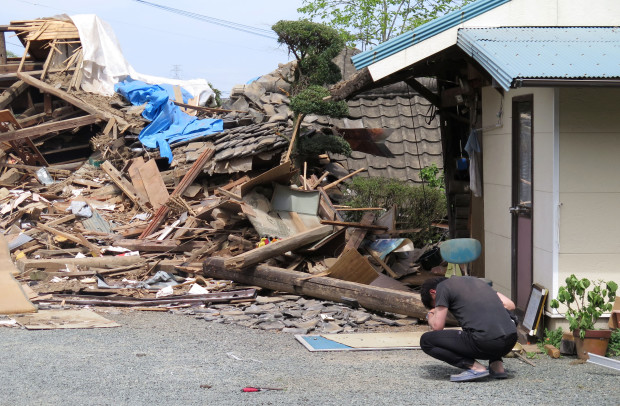 A man hunks down in front of a collapsed residence where his mother is being trapped after an earthquake in Mashiki, Kumamoto prefecture, southern Japan, Saturday, April 16, 2016. Powerful earthquakes a day apart shook southern Japan, trapping many beneath flattened homes and sending thousands to seek shelter in gymnasiums and hotel lobbies. (Kyodo News via AP) JAPAN OUT, MANDATORY CREDIT