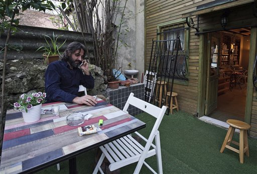 In this photo taken on Friday, April 1, 2016, Syrian refugee Samer Al-Kadri, founder and owner of Pages, a rustic three story-Arabic language bookshop, sits outside his store in Istanbul, Turkey. The bookstore has become an anchor for many Syrians who have stayed put in Turkey but crave a taste of home. Al-Kadri, a refugee himself, says the store strives to be a bridge between Syrians, Turks and the myriad of foreigners who visit the city. Its weekly program includes oriental music concerts and, starting soon, language exchanges in Arabic, English and Turkish. Books are available in all three languages. (AP Photo/Bram Janssen)