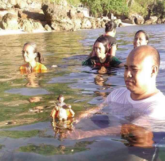 Six Filipinos stand chest deep in a river.  The man in front holds an eight inch Santo Nino statue.