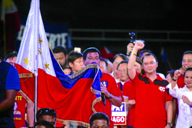 Mayor Rodrigo Duterte kisses the Philippine flag during his meeting de avance in Luneta Park. PHOTO BY MARIANNE BERMUDEZ